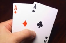 Human hand holding an ace of diamonds and an ace of clubs against a dark background