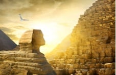 An image of the Egyptian Sphinx, one wall of the Great Pyramid of Giza and a bird in flight against a golden cloudy sky