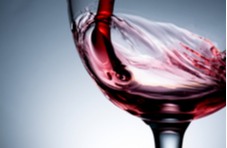 A close-up image of red wine being poured into a glass against a blueish background