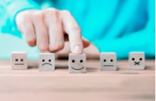 A range of emoticons on little wooden cubes on a wooden surface with a male hand pointing to the smiling emoticon