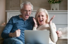 middle aged couple sitting on the sofa winning playing online slots on their laptop