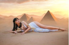 An image of a richly adorned Cleopatra lying on the desert sands with the pyramids as a backdrop