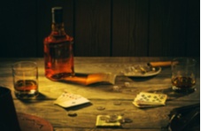 A wooden table with two hands of poker cards laid out, a cigar, banknotes, coins, and bourbon against a dark background