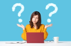 An image of a women in front of a laptop with her hands outstretched and large white question marks in each side.